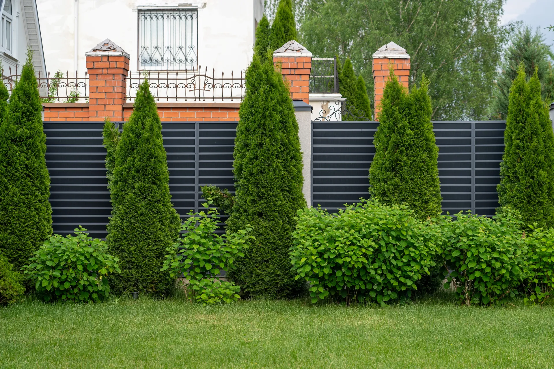 Dark aluminum privacy fence with brick pillars and landscaping